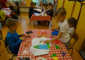Trójka dzieci wykleja kontur Polski wyciętymi elementami z papieru.
